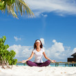 Pretty woman doing yoga exercises on the tropical  beach