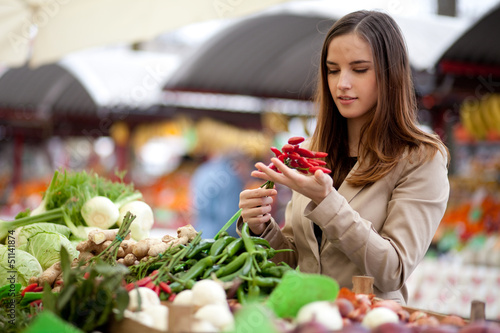Photo: Young woman buying red hot chilli peppers at the market Young woman buying red hot chilli peppers at the market