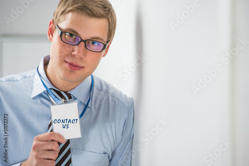 Photo: Handsome businessman showing "contact us" text on a badge Handsome businessman showing "contact us" text on a badge