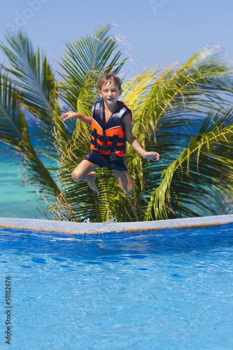 Photo: young happy boy jumping in swimming pool on tropical background young happy boy jumping in swimming pool on tropical background