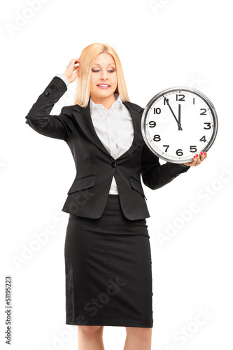 Photo: A young businesswoman holding a wall clock in her hand and gestu A young businesswoman holding a wall clock in her hand and gestu