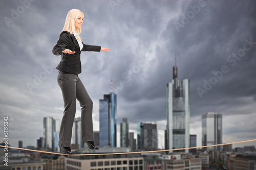 Photo: Businesswoman walking on a rope, with Frankfurt in the backgroun Businesswoman walking on a rope, with Frankfurt in the backgroun