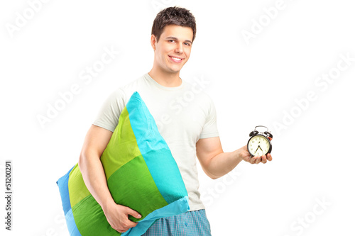 Photo: A smiling man in pajamas holding a pillow and alarm clock A smiling man in pajamas holding a pillow and alarm clock