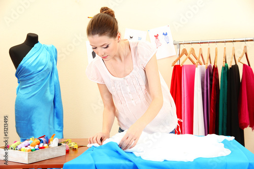 Photo: beautiful young dressmaker in workroom beautiful young dressmaker in workroom