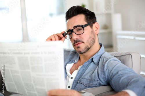 Photo: Cheerful guy reading newspaper in sofa Cheerful guy reading newspaper in sofa