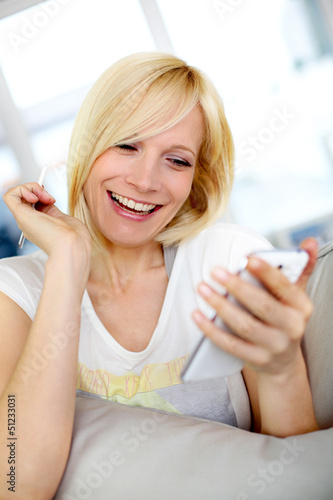 Photo: Smiling young woman at home using smartphone Smiling young woman at home using smartphone