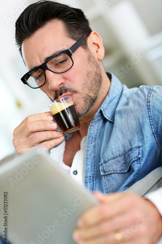 Photo: Man with glasses drinking coffee and using tablet Man with glasses drinking coffee and using tablet