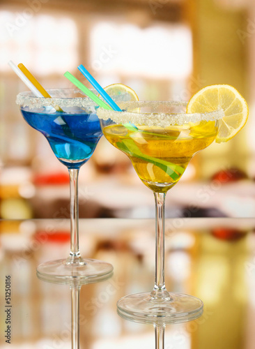 Photo: Yellow and blue cocktails in glasses on room background Yellow and blue cocktails in glasses on room background