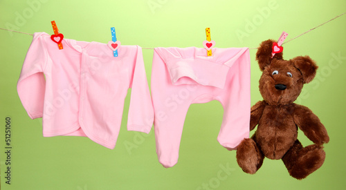 Photo: Baby clothes hanging on clothesline, on color background Baby clothes hanging on clothesline, on color background