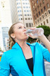 Woman Drinking Water Whilst Running Along Urban Street