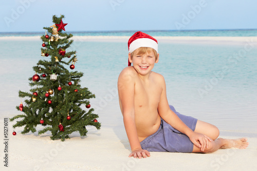 Photo: Boy Sitting On Beach With Christmas Tree And Hat Boy Sitting On Beach With Christmas Tree And Hat