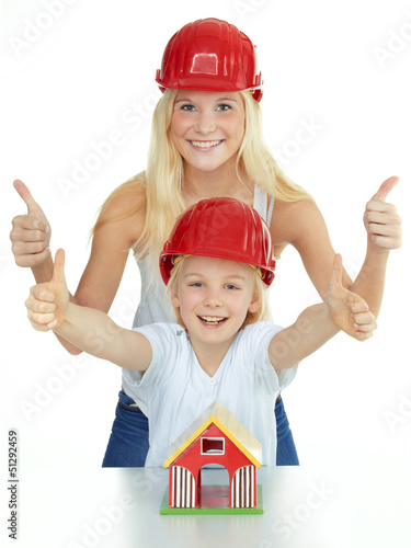 Photo: Two girls with helmet shows thumbs up for building a house Two girls with helmet shows thumbs up for building a house