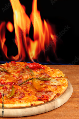 Photo: Tasty pepperoni pizza on wooden board on flame background Tasty pepperoni pizza on wooden board on flame background