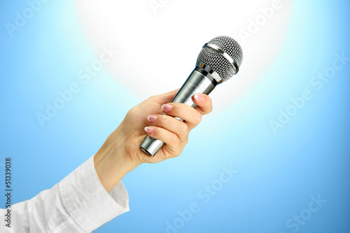 Photo: female hand with microphone, on blue background female hand with microphone, on blue background