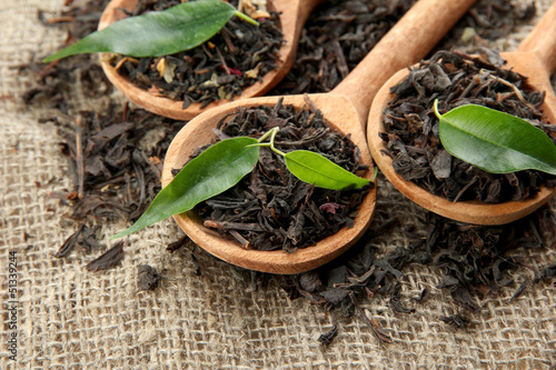 Photo: Dry tea with green leaves in wooden spoons, on burlap Dry tea with green leaves in wooden spoons, on burlap