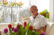 Senior man with glasses reading book in living room.