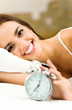 Photo: Woman with alarmclock on the bed Woman with alarmclock on the bed