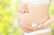 Pregnant woman applying skin care cream on belly over green