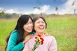 Smiling daughter and her mother with carnation flower on the gra