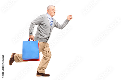 Photo: Full length portrait of a smiling gentleman running with shoppin Full length portrait of a smiling gentleman running with shoppin