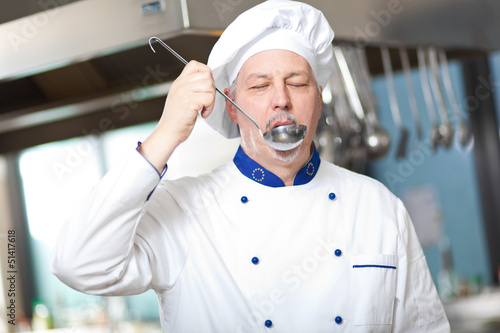 Photo: Smiling chef smelling the soup in kitchen Smiling chef smelling the soup in kitchen