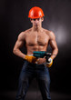 Muscular worker with an electric drill on a black background.