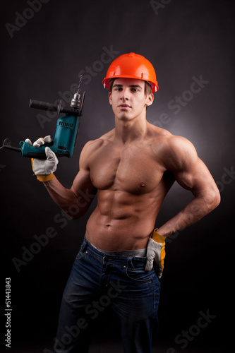 Photo: Muscular worker with an electric drill on a black background. Muscular worker with an electric drill on a black background.