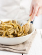 Cook mixing pesto with penne rigate pasta