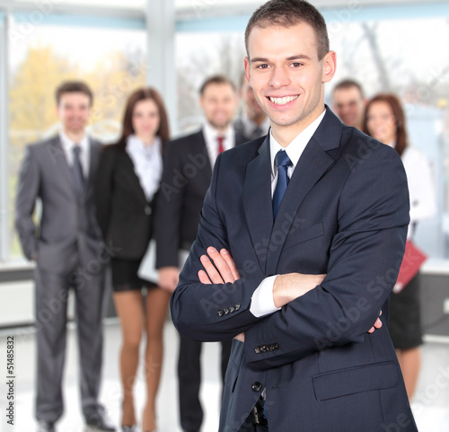 Photo: Handsome happy business man with colleagues at the back Handsome happy business man with colleagues at the back