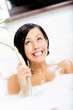 Woman lying in bathtub with suds plays with shower head