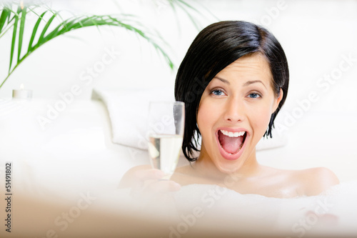 Photo: Woman taking a bath with suds drinks champagne Woman taking a bath with suds drinks champagne