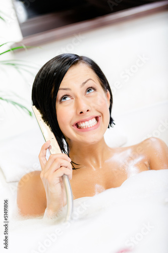 Photo: Woman lying in bathtub with suds plays with shower head Woman lying in bathtub with suds plays with shower head