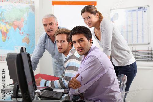 Photo: Group of casually dressed people working round a computer Group of casually dressed people working round a computer