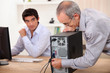 old man plugs a computer under the watch of a young man