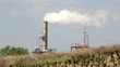 Smoking industrial chimney behind a field in front of sky