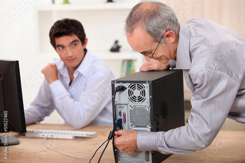 Photo: old man plugs a computer under the watch of a young man old man plugs a computer under the watch of a young man