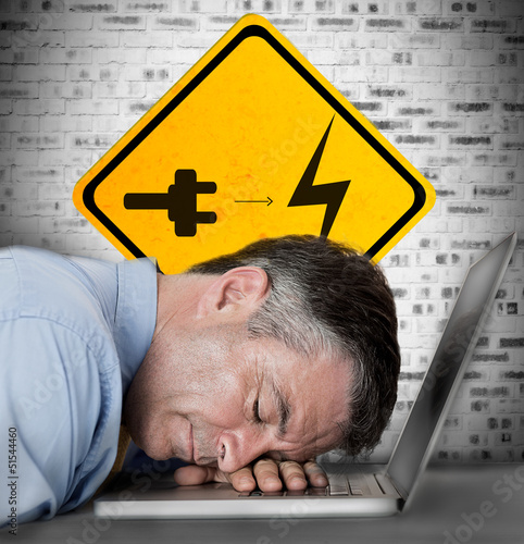 Photo: Businessman sleeping on his laptop with battery plug roadsign Businessman sleeping on his laptop with battery plug roadsign