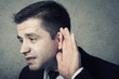 Business man holding his hand to his ear trying to hear