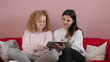 Two female friends sitting on the sofa with tablet computer
