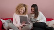 Two female friends chatting on tablet computer, indoors