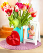 Beautiful tulips in bucket with gifts on table in room