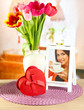 Beautiful tulips in bucket with gifts on table in room