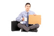 Unhappy young businessman sitting on floor with a piece of cardb