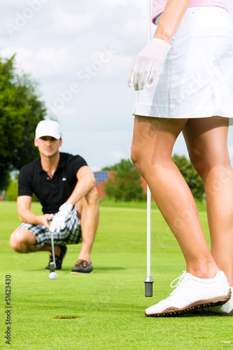 Photo: Young sportive couple playing golf on a course Young sportive couple playing golf on a course