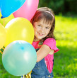 Little happy girl holding colorful balloons in green park