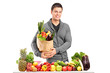 Handsome young man with a bag of groceries standing behind a pil