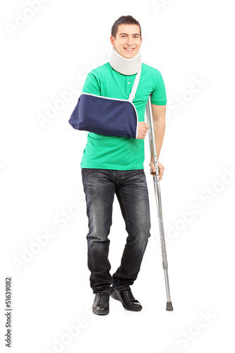 Photo: Full length portrait of a smiling male with broken arm and crutc Full length portrait of a smiling male with broken arm and crutc
