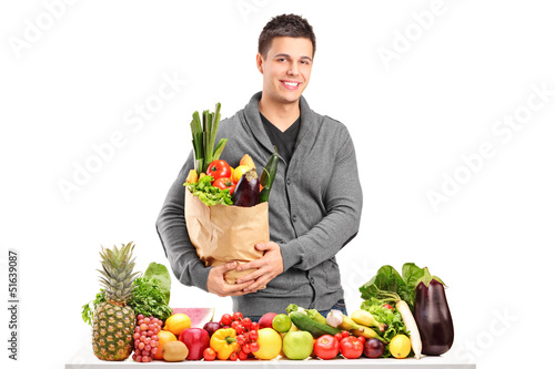 Photo: Handsome young man with a bag of groceries standing behind a pil Handsome young man with a bag of groceries standing behind a pil