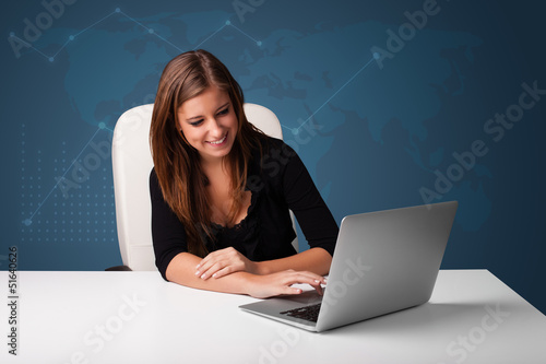 Photo: Young woman sitting at desk and typing on laptop Young woman sitting at desk and typing on laptop