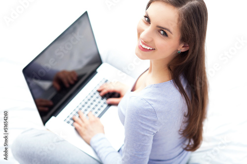 Photo: Woman sitting on bed with laptop Woman sitting on bed with laptop